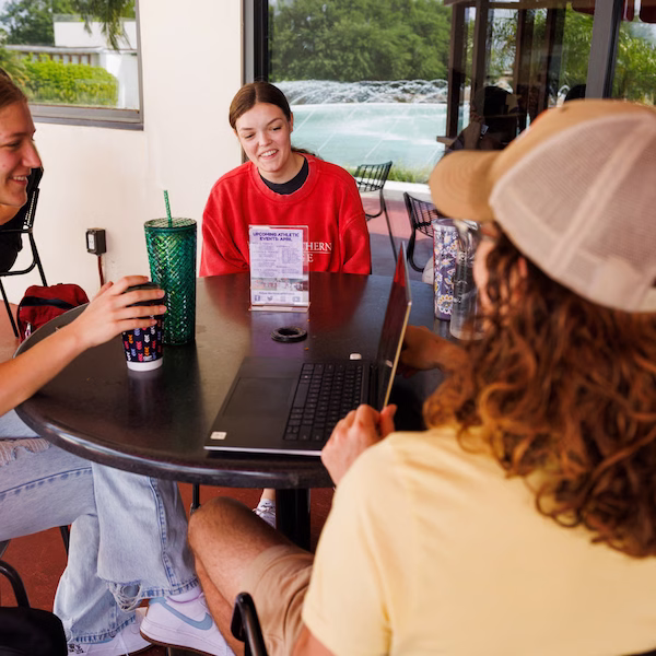 Students drinking coffee at a round table with a laptop