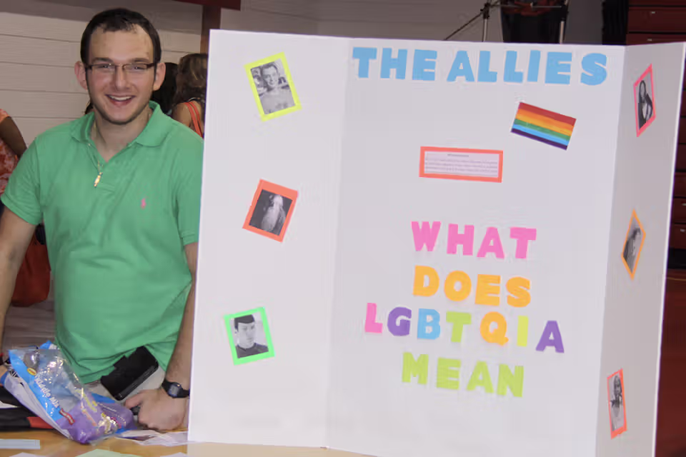 Student smiling next to poster board explaining the Allies club