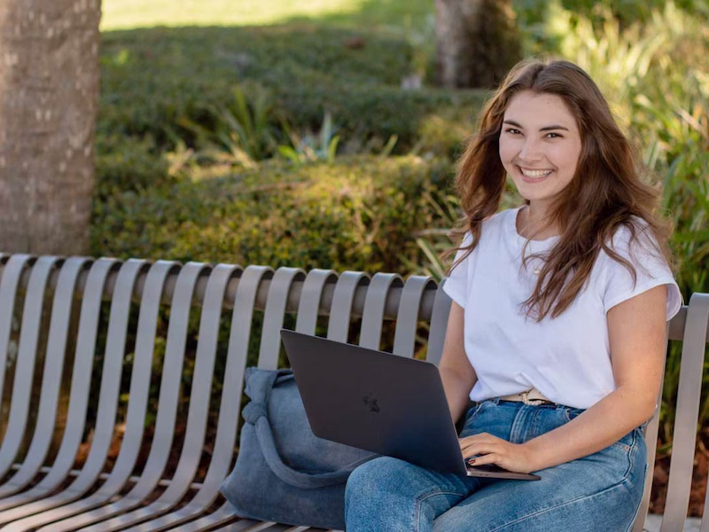 Student sitting outside on bench with laptop