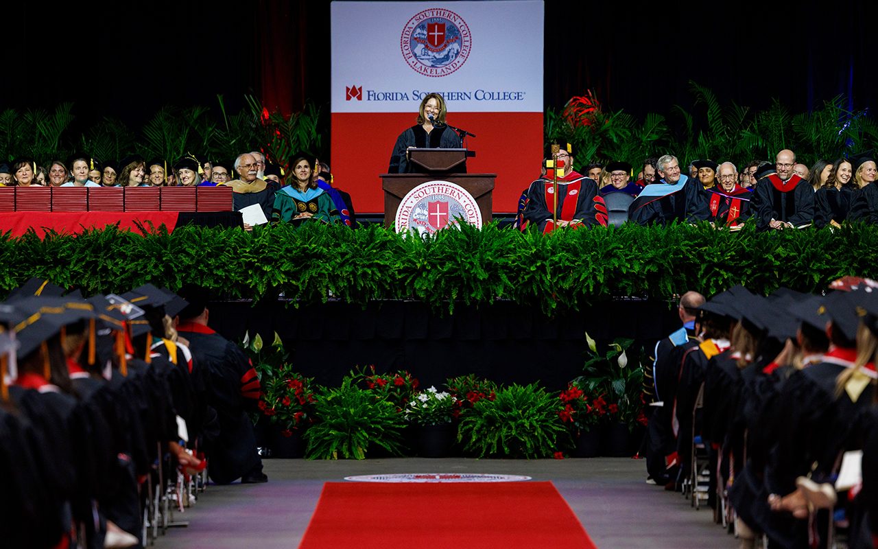 students sitting at graduation while Mccarley stands at podium on stage